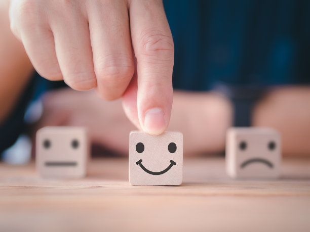 顾客满意度调查概念。近距离客户手在木方上选择快乐的笑脸、模糊的中性和悲伤的脸图标来调查反馈、评分、评论、服务满意度。图片下载