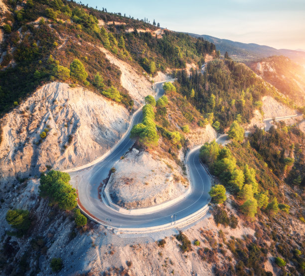鸟瞰希腊夏季的山路、日落时的绿色森林。俯视图从无人机的道路在森林。美丽的风景，山道，松树，春天的白石。旅行图片下载