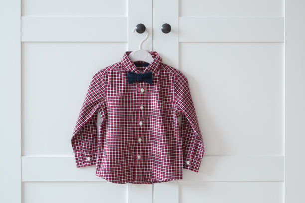 红白格子新婴儿衬衫与深蓝色领结挂在衣柜门把手的衣架上。特写镜头。前视图。为聚会、节日或其他庆祝活动准备的衣服。图片下载