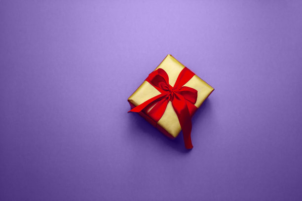 节日礼物。盒子在一个金色的礼物包装与红色的蝴蝶结，在粉红色的背景。祝你圣诞、情人节快乐。用爱的明信片。图片下载
