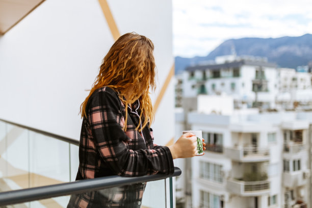 一个年轻的黑发女人穿着睡衣，在温暖的阳光下享受着她的早茶。城市的生活方式图片下载