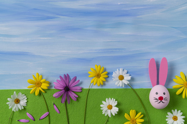 在绿色毛毡和蓝色天空上画复活节彩蛋和复活节兔子的脸图片下载