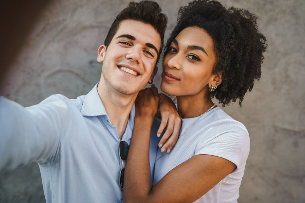 黑白混血的男女朋友在灰色的墙壁背景下自拍，一个女孩把手放在她男人的肩膀上图片下载