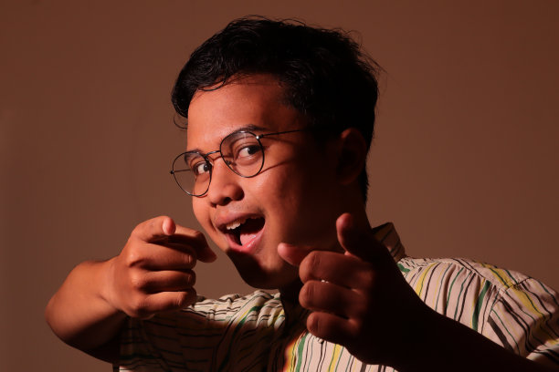 穿着休闲衬衫的亚裔年轻男子用食指指指点点。微光像人像图片下载