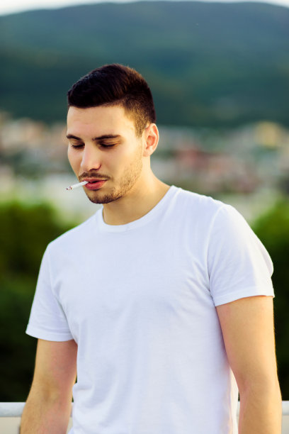 英俊潇洒的年轻人在夏天的时候在外面吸烟图片下载
