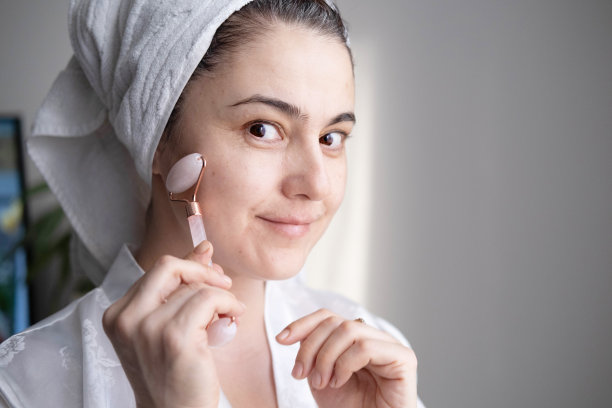 这是一个年轻女子的特写照片，她看起来很放松，面带微笑，正在用天然玫瑰石英石做的面部按摩。图片下载