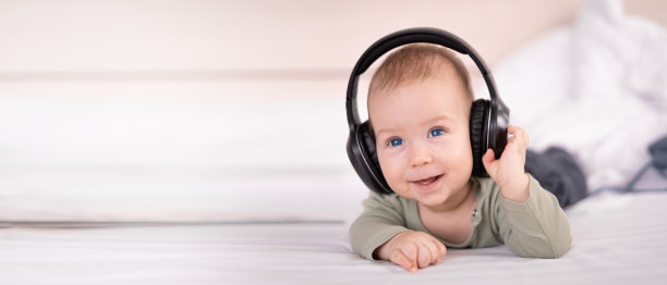 笑着的宝宝躺在床上听音乐，戴着耳机，无线耳机进行教育，4个月大的宝宝在白色背景上图片下载