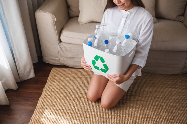 一个女人收集和持有一个可回收的垃圾塑料瓶在家里的垃圾桶的特写图像图片下载