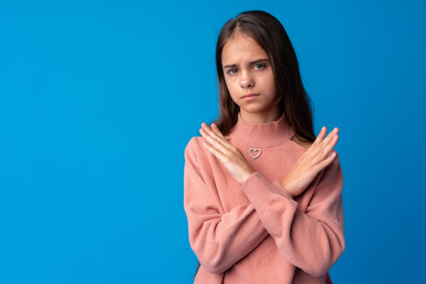 年轻漂亮的少女在蓝色背景下交叉双臂，做出否定手势图片下载