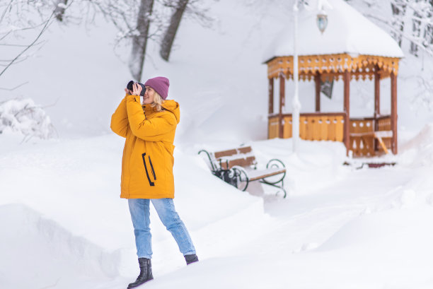 穿着黄色夹克的快乐女孩摄影师在雪地公园拍摄冬天的照片图片下载