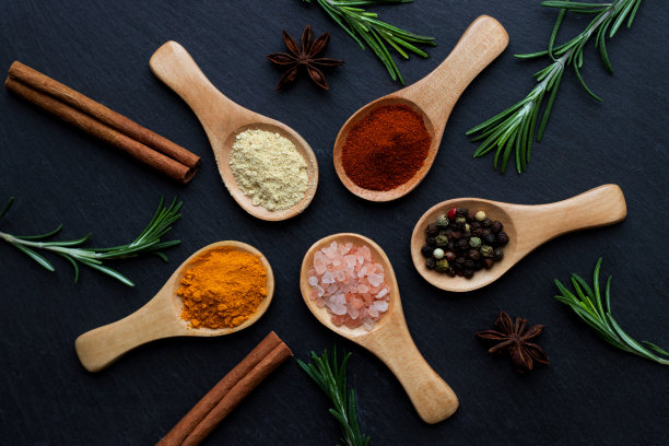 在深色的桌子上，用木勺将各种各样的香料、香草、新鲜的迷迭香和粉红色的喜马拉雅盐组合在一起。俯视图图片下载