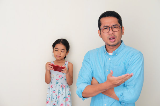 当女儿在后面玩手机时，一名亚裔父亲露出忧虑的表情图片下载