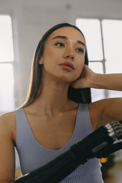 20多岁的漂亮女孩在健身房用仿生假肢，紧张的训练训练后休息，在蓝色的窗口摆姿势。健康的生活方式。生物工程图片下载