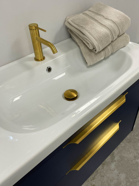 现代浴室与灰色梳妆台顶部白色，陶瓷水槽与黄金龙头龙头和堆叠折叠的米色毛巾的特写图像图片下载