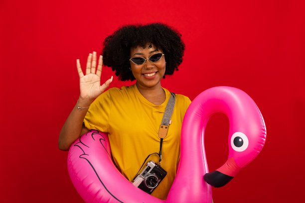 美丽的非洲和亚洲妇女微笑着抱火烈鸟橡胶环，享受他们的暑假粉红色背景孤立。快乐的旅行概念。图片下载