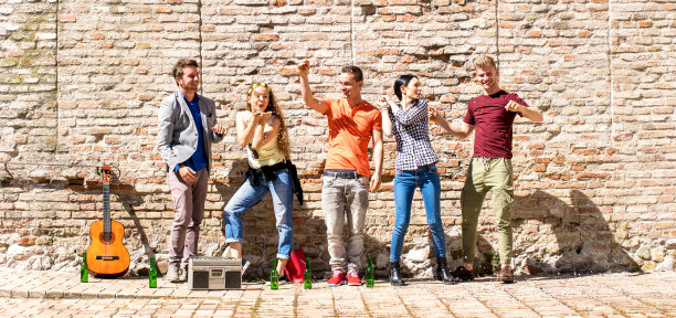 千禧一代的朋友们在户外用五彩纸屑和啤酒瓶欢呼，快乐的人们在城市聚会上一起享受春天，明亮生动的过滤器上的青年生活方式概念图片下载