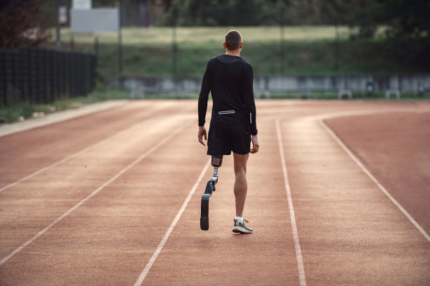 一名戴着假腿的运动员在体育场跑道上行走的后视图。图片下载