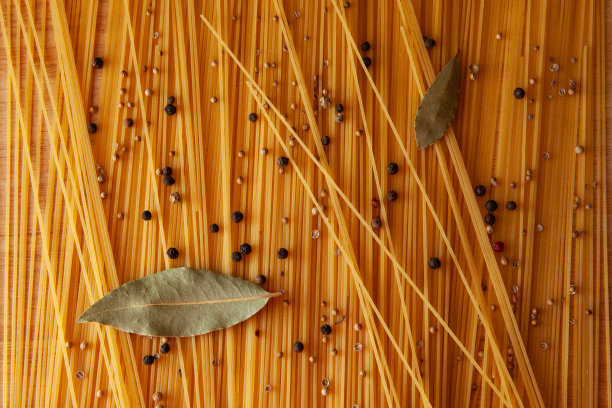 食物主题:生意大利面作为整个背景。黄色的意大利面和黑胡椒豌豆散落在桌子上，用于出版物、海报、日历、邮件、屏保、壁纸、明信片、卡片、横幅、封面图片下载