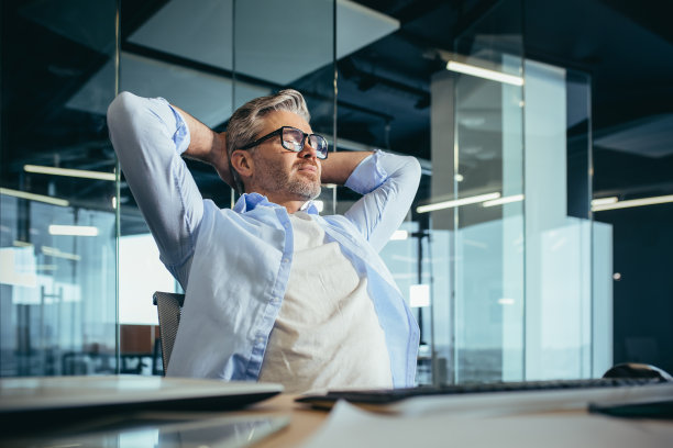 沉思和梦幻的经验丰富的商人老板，坐在工作，把他的手放在脑后，休息图片下载