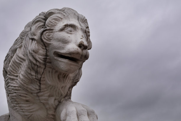 一个大的白色石狮的特写照片在一个秋天阴暗和多云的天空。圣彼得堡的公园里树立了一座雕像。风化和老化的图形覆盖裂缝图片下载