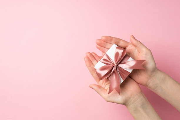 第一人称俯视图照片的saint valentine's day装饰年轻女子的手给小白色礼品盒粉红色丝带蝴蝶结在孤立的淡粉色背景copyspace图片下载