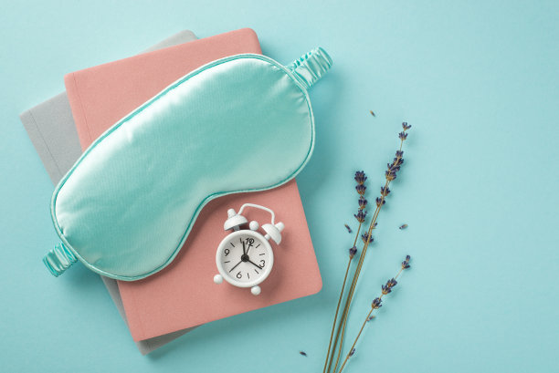俯视图照片的蓝色丝绸睡眠面具小白色闹钟的规划者和小枝薰衣草在孤立的柔和的蓝色背景与copyspace图片下载