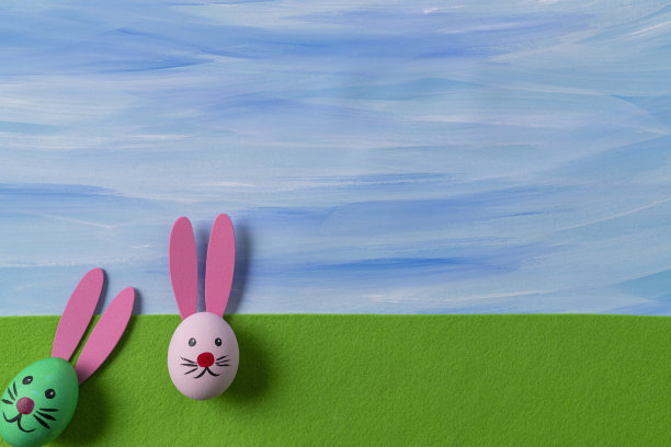 在绿色毛毡和蓝色天空上画复活节彩蛋和复活节兔子的脸图片下载