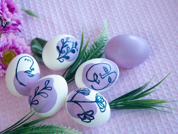 复活节彩蛋、小草小枝和绿叶的美丽组合。鸡蛋上绘有紫色的花卉装饰和人脸。文本的地方图片下载