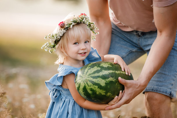年轻的父亲和小女儿享受家庭野餐在美丽的夏季公园举行大西瓜。与父亲共度周末概念素材图片
