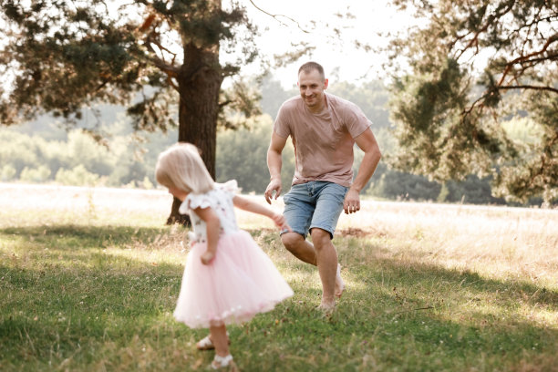 夏天，爸爸和小女儿玩。爸爸和孩子在一起的照片。爸爸，小女儿在户外。年轻的父亲带着小女儿在公园散步。家庭假日在花园或森林。图片下载