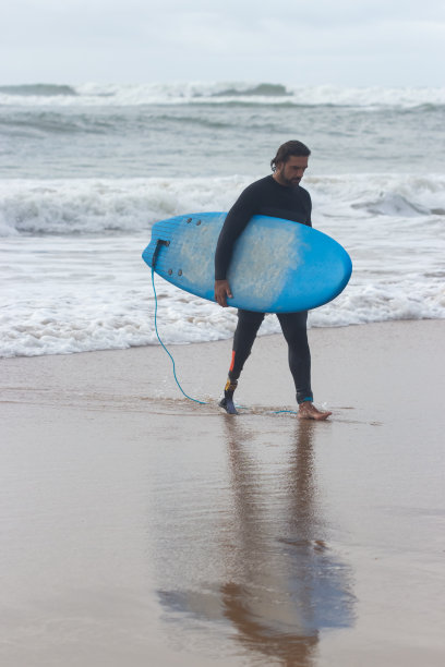 一个留着胡子和卷发的男人走在沙滩上图片下载
