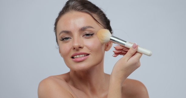 美丽的女人与完美的化妆肖像。她用化妆刷在脸上搽脂粉。美妆概念。图片下载