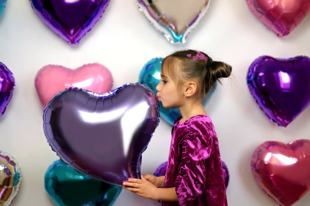 身着紫色连衣裙的女孩亲吻背景上的心形气球图片下载