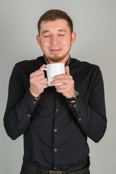 一位留着胡子的商人穿着一件黑色衬衫，手里拿着一个白色的杯子，里面放着热饮，他正享受着咖啡的香味图片下载