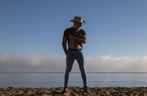 一个戴着牛仔帽和牛仔裤的成年人，在海边和天空的映衬下。西班牙阿尔梅里亚图片下载