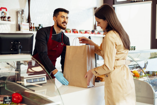 在杂货店为女顾客搬运购物袋的店员图片下载