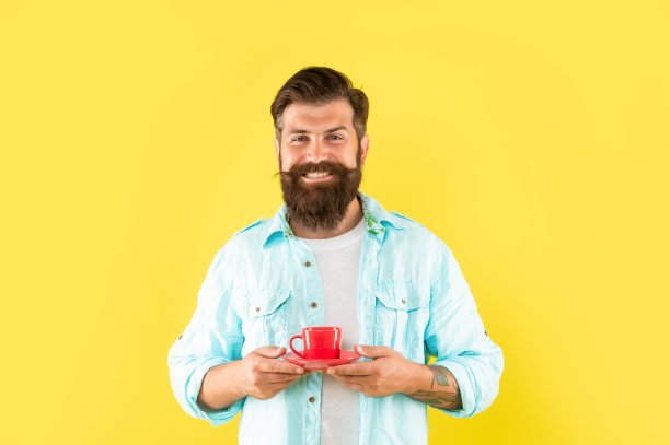 严肃的大胡子男人喝着黄色背景的咖啡，早上好图片下载