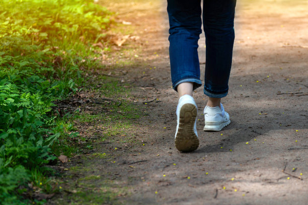一位身穿白蓝相间牛仔裤的年轻女子正走在公园的碎石小道上。夏季散步、娱乐和消遣。休闲的生活方式。图片下载