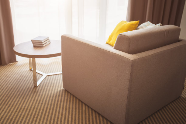 明亮的大窗户旁有靠枕的软垫扶手椅，咖啡桌上放着一堆书图片下载