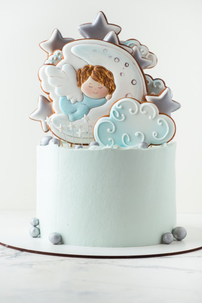白色背景上装饰着姜饼饼干的蓝奶油芝士糖霜洗礼蛋糕。小天使睡在月亮上。图片下载