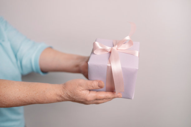 近距离拍摄的女性的手，紫色的礼物包裹着粉红色的丝带。图片下载