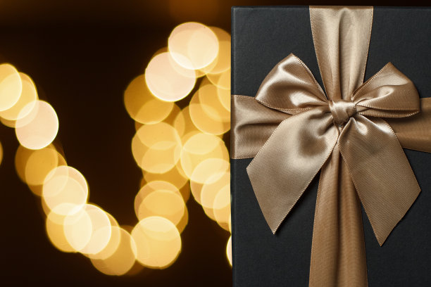 黑色礼盒与一个黄色花环背景上的金色蝴蝶结。背景是黄色散景图片下载