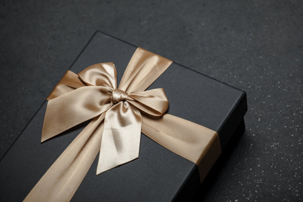 黑色礼盒与一个金色的丝带和一个大蝴蝶结花岗岩黑色背景。图片下载