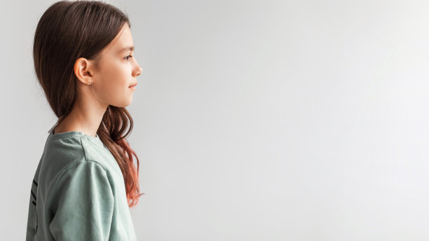 侧视图严肃的女孩站在一边看，灰色的背景图片下载