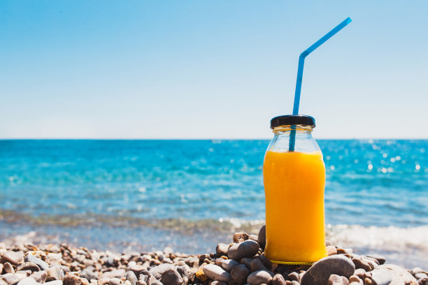 在大海的背景下，一杯装在玻璃瓶里的黄色橙汁图片下载
