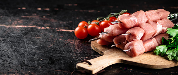 在切菜板上的生猪肉串，配上西红柿和香草。图片下载