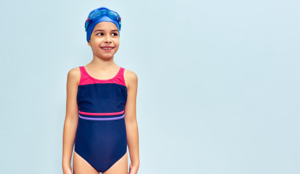 可爱的小女孩穿着泳装，头戴护目镜，腰部戴着充气环跳在空中，在蓝色的工作室背景下被孤立。暑假是学校放假的概念。一个小女孩戴上了一副可爱的儿童泳镜图片下载