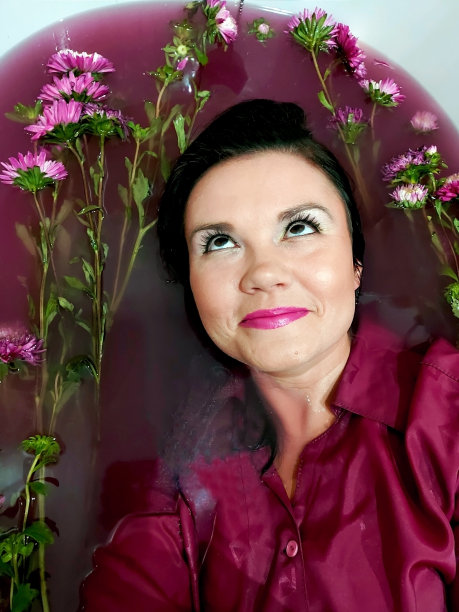 时尚内饰照片性感美丽的女人与黑色的头发躺在菊花花瓣在浴缸。美丽的女孩在紫色，紫色，粉红色，非常围水在菊花沐浴。恢复和放松的概念图片下载