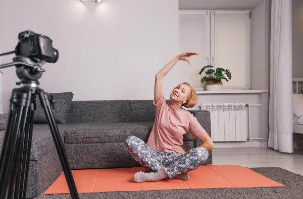 一位上了年纪的妇女，一个博客作者在家里参加在线瑜伽课程，这是一种老年人健康生活方式的概念。图片下载