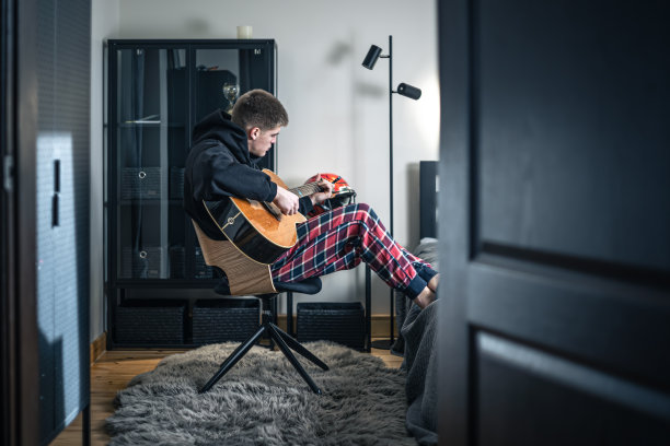 一个年轻人在家里的房间里弹着原声吉他。图片下载